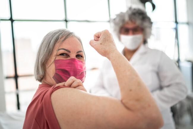Woman being vaccinated and flexing biceps muscle – wearing face mask