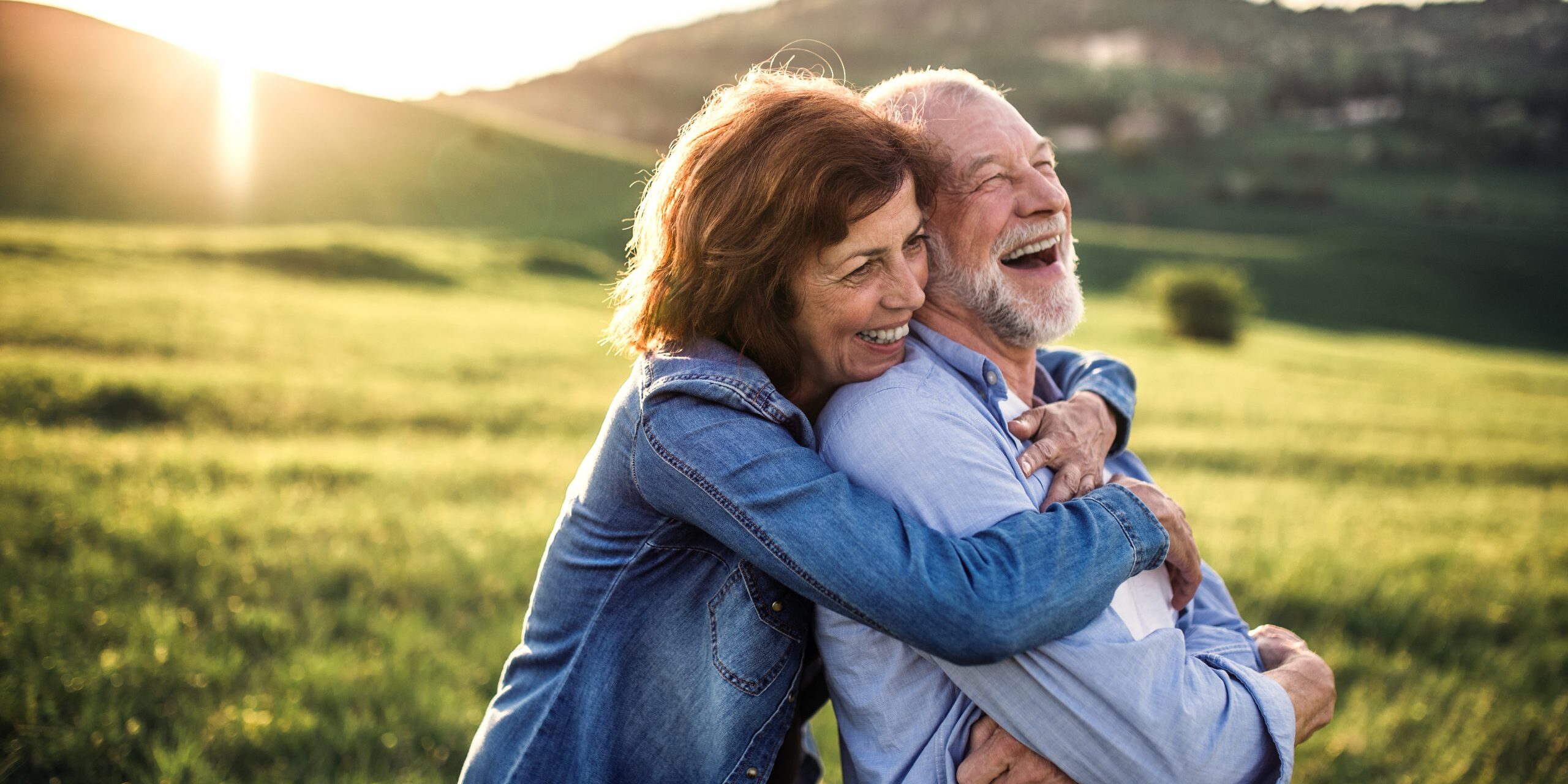 Side view of senior couple hugging outside in spring nature at sunset.