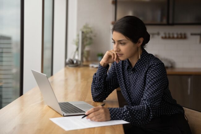 Pensive Indian woman work online on laptop