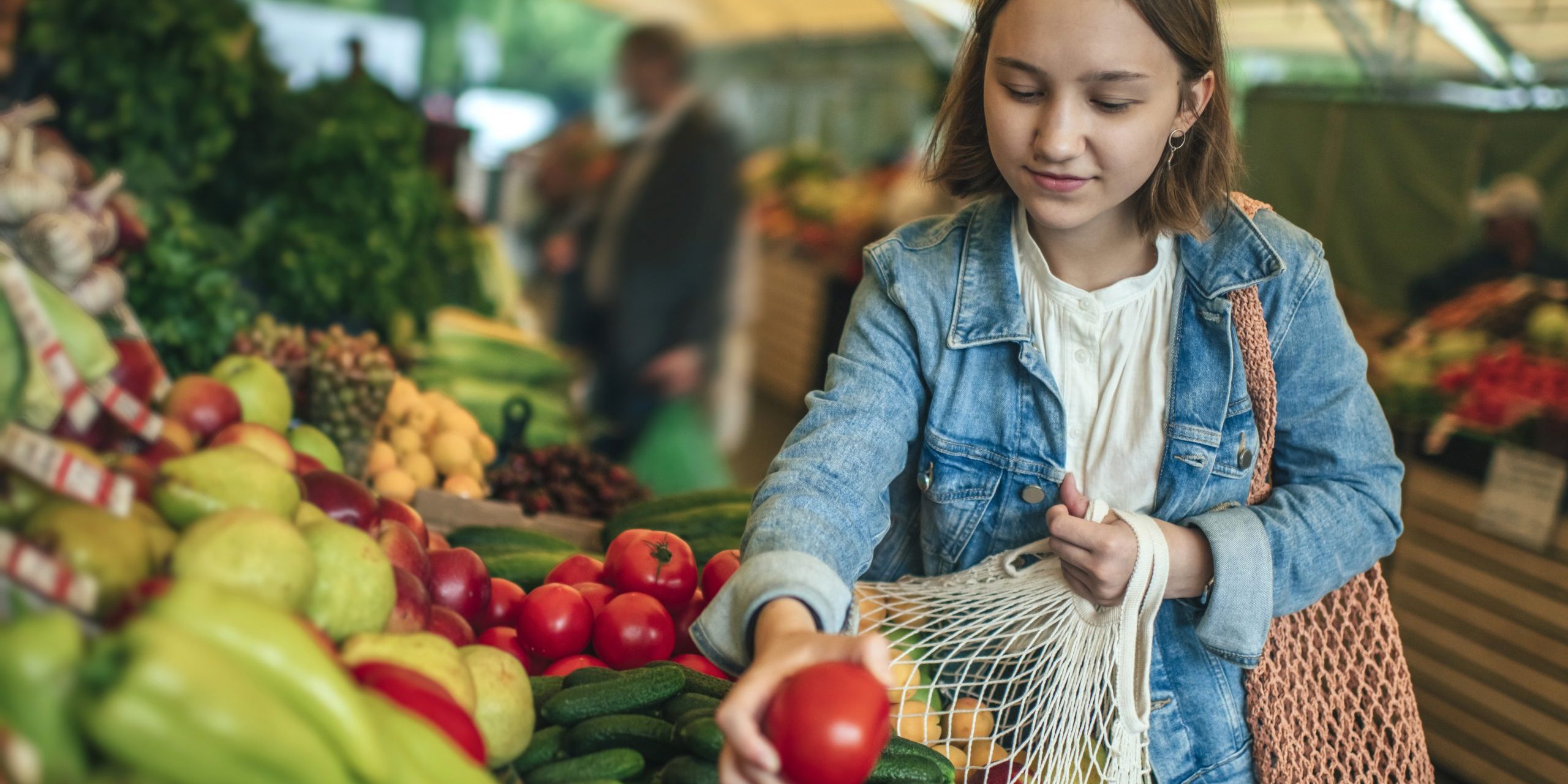 Young girl choosing vegetables and fruit at a farmers market with reusable bag, plastic free and zero waste concept