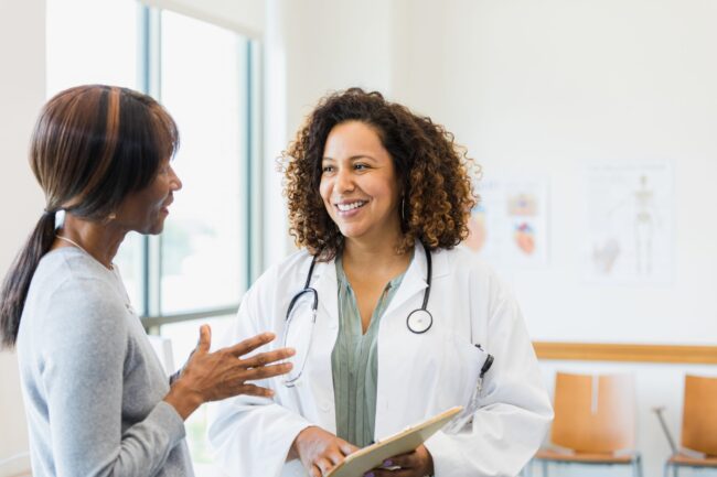 Standing together, female doctor smiles while mature female patient speaks