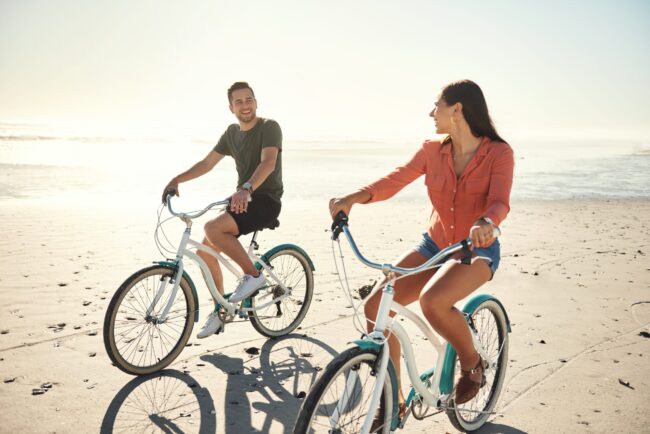 Two people young caucasian couple happy smiling enjoying riding bicycles on holiday at the beach