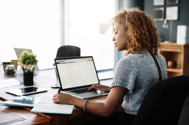 Young businesswoman taking notes on changing compliance regulations. Shot of a young businesswoman working on a laptop in an office
