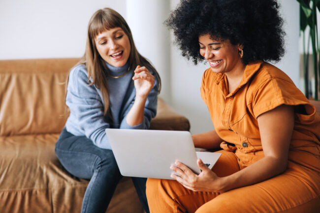 Discussing benefits. Cheerful young businesswomen smiling happily while using a laptop together. Two female entrepreneurs working as a team in a modern workplace.