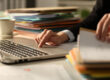 Close up of executive hands working hard late hours using laptop in the night at office checking a pile of documents