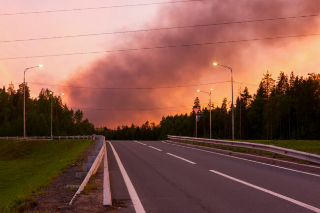 Black smoke from a fire in crimson sunset sky over the road in summer Black smoke from a fire in the crimson sky from the sunset over the road in summer