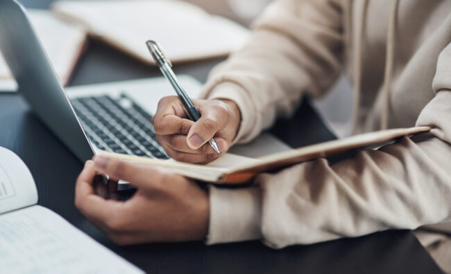 Taking notes on compliance updates. Shot of an unrecognisable man writing in a notebook while working from home