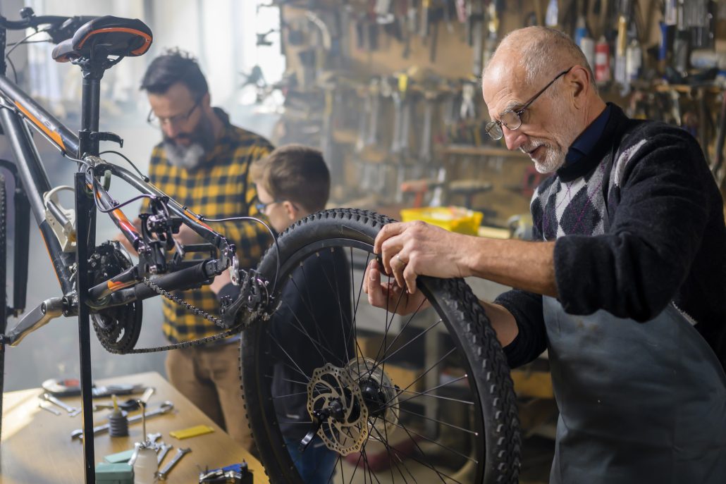 Senior man repairing bicycle while father and son standing in background.