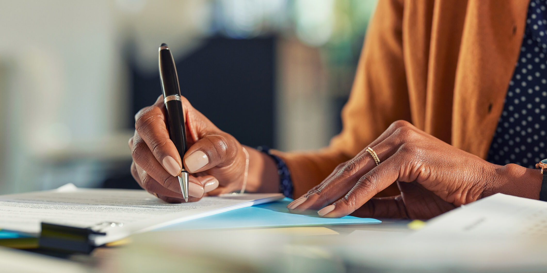 African business woman hand writing on paper at desk Close up of african american business woman hands writing on report while working in office. Successful black woman signing documents at home using a pen. Mid adult freelancer signing contract document on table.