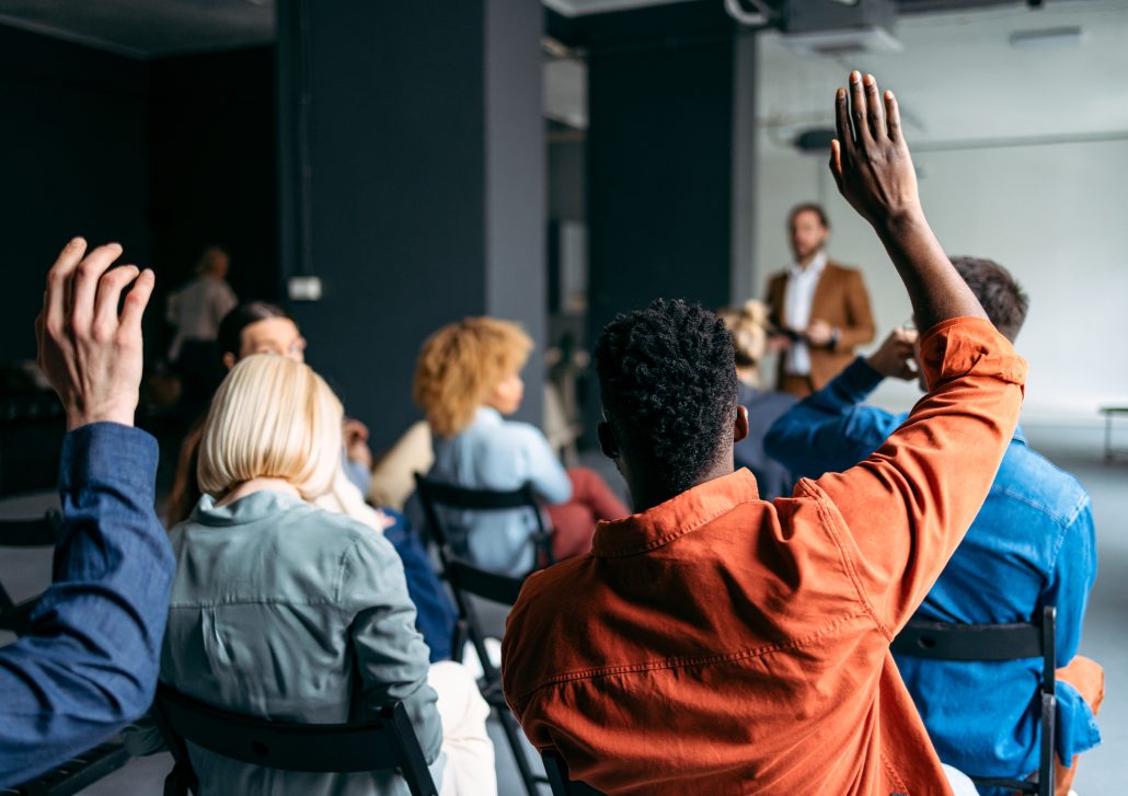 Unrecognizable group of multi-ethnic businesspeople raising their hands during a presentation at their company.