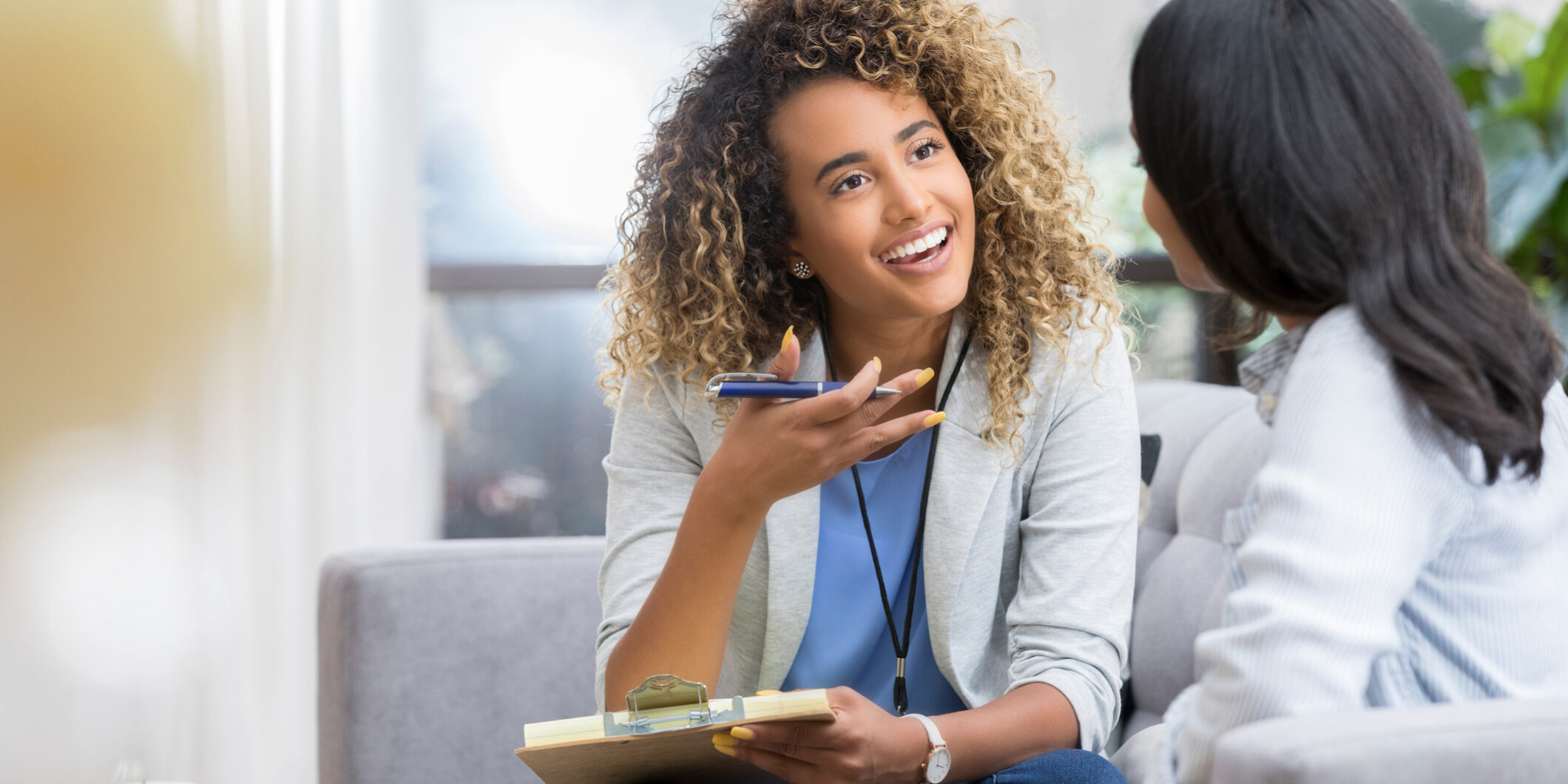 Encouraging therapist talks with young woman Positive young female therapist gestures as she talks with a female client. The therapist smiles warmly as she talks with the young woman.