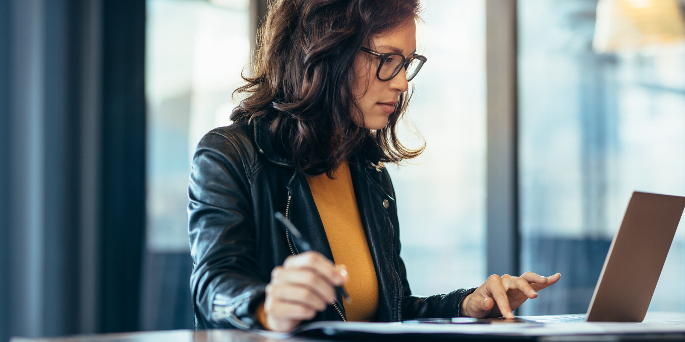 Businesswoman making notes looking at a laptop