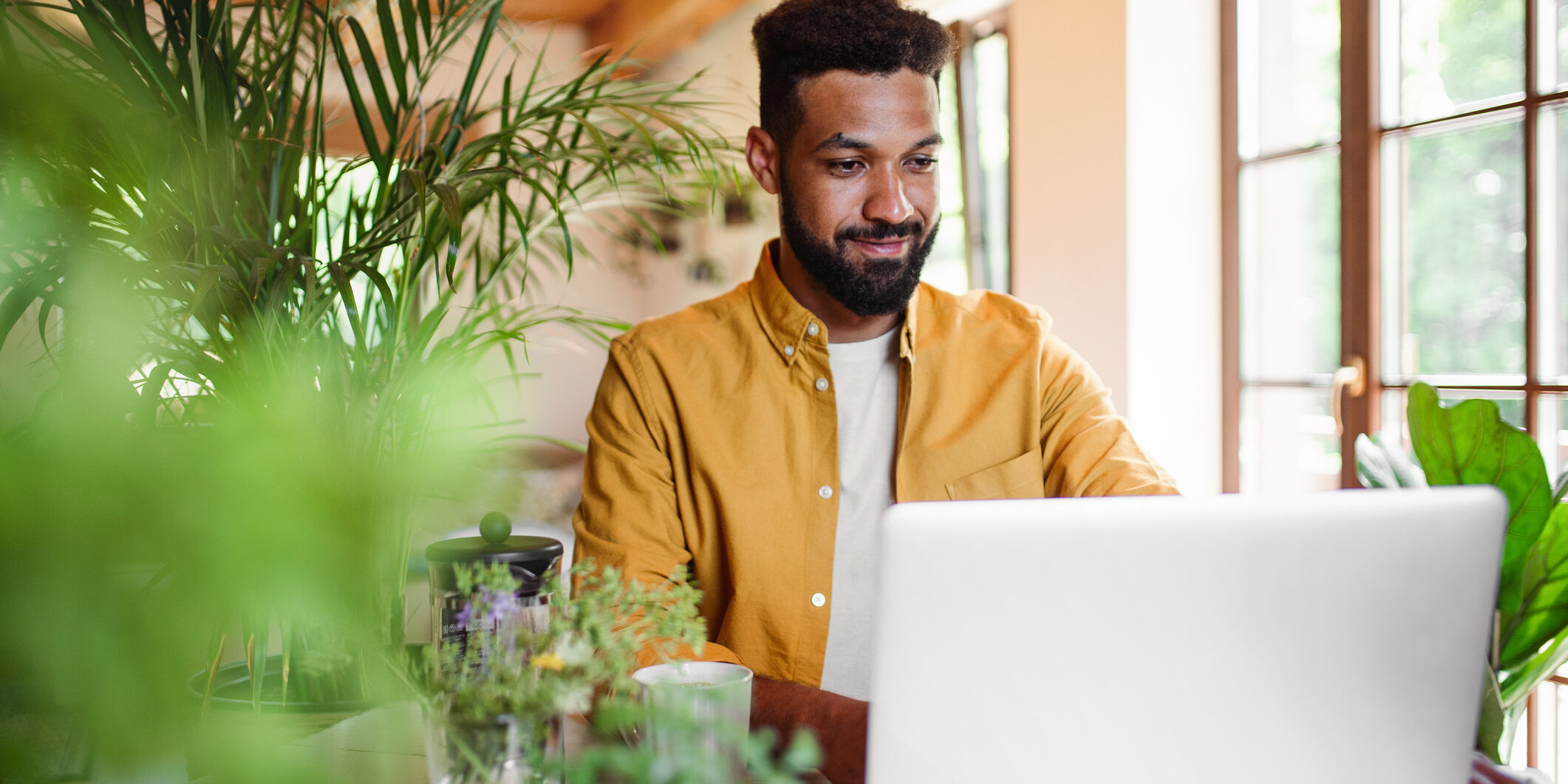 Young man with laptop and coffee working indoors, home office concept.