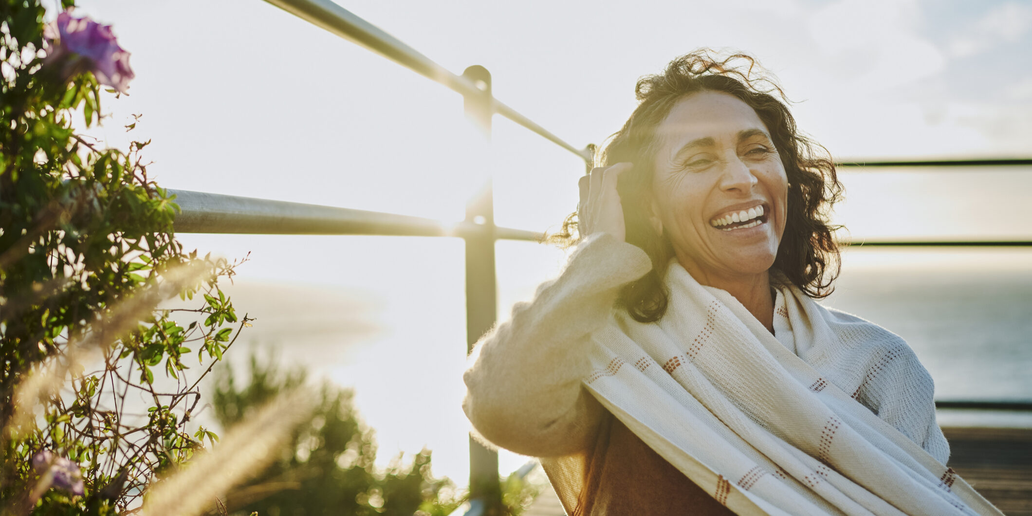 Laughing mature woman sitting by the ocean at sunset