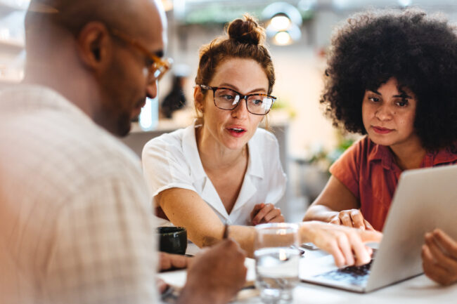 Business women having a discussion with a client over a business lunch Business women having a work lunch in a café, exchanging ideas and discussing their projects with a client. Young business team using a laptop as they sit around a coffee table.