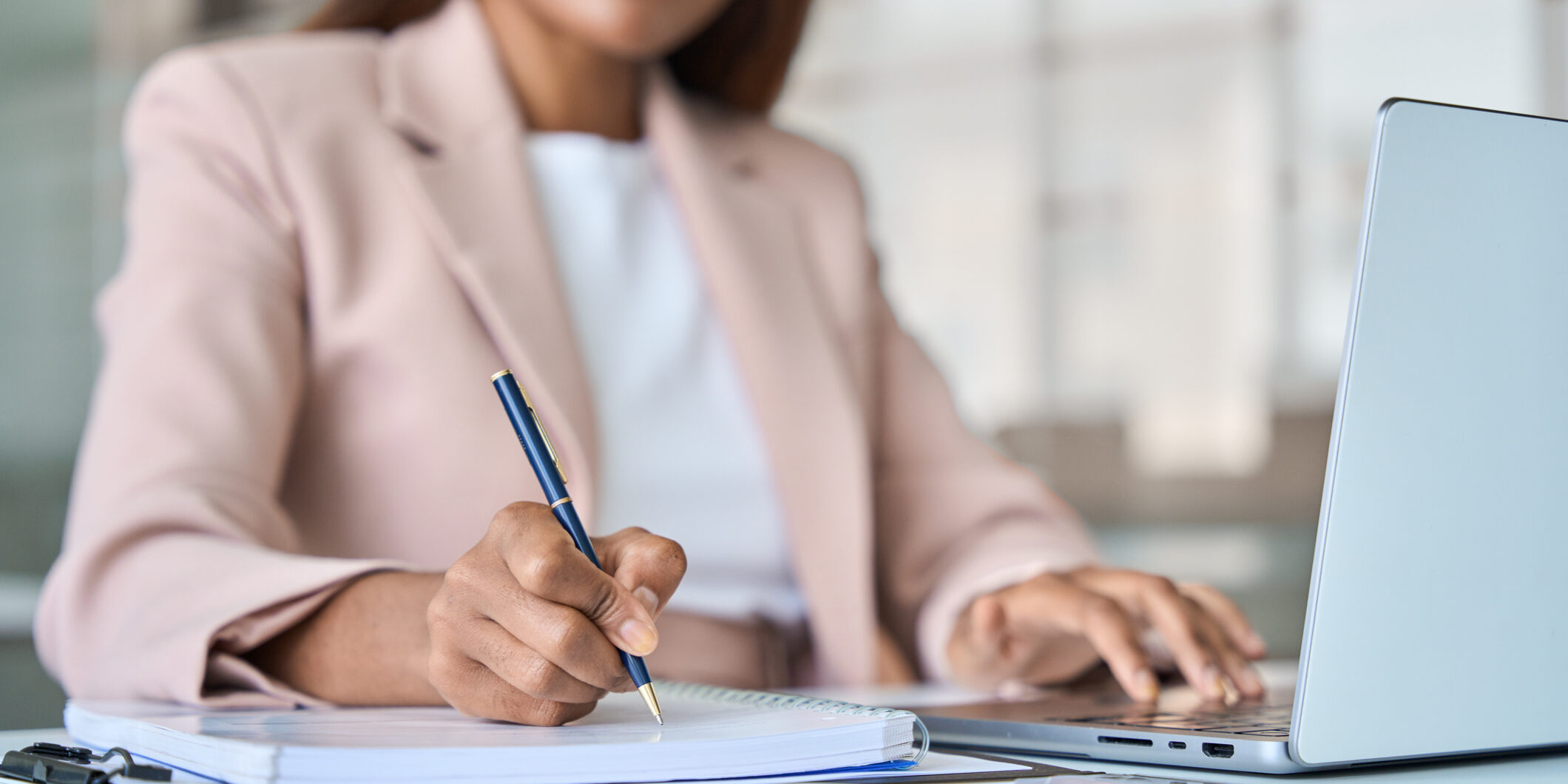 Close up view of professional business woman working writing notes in notebook. Close up view of professional busy African American business woman manager executive working on laptop computer writing notes in notebook at work elearning in corporate office.
