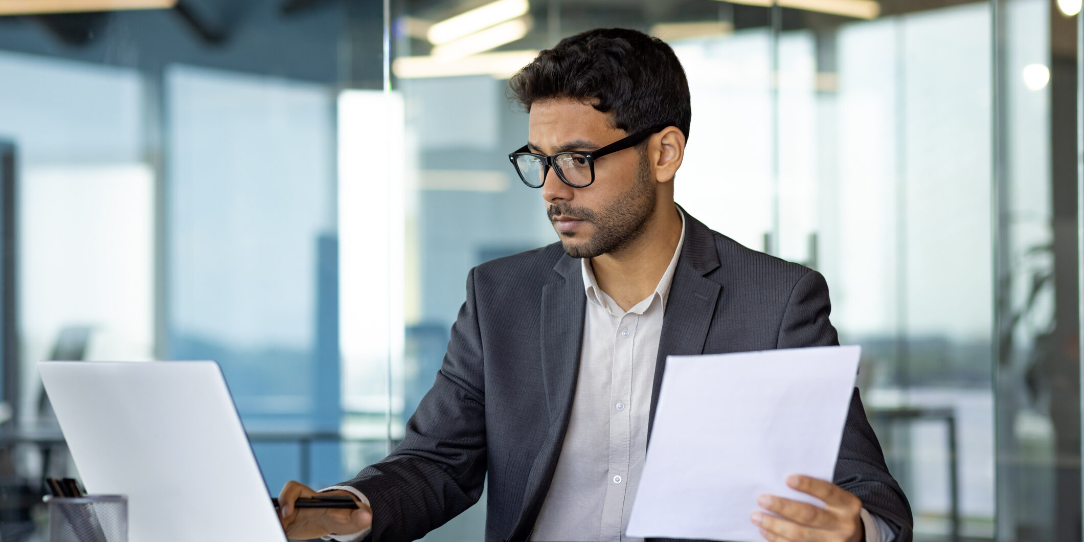 Serious concentrated hispanic businessman financier on paperwork inside office, man in business suit at workplace reviewing and reading papers, contracts and accounts reports.
