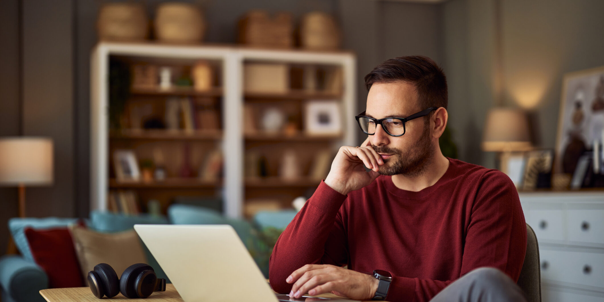 A busy young adult male freelancer resting his head on his hand while working on a project on a laptop. A busy, focused young adult male freelancer sitting at a desk and resting his head on his hand while working on a project on his laptop.