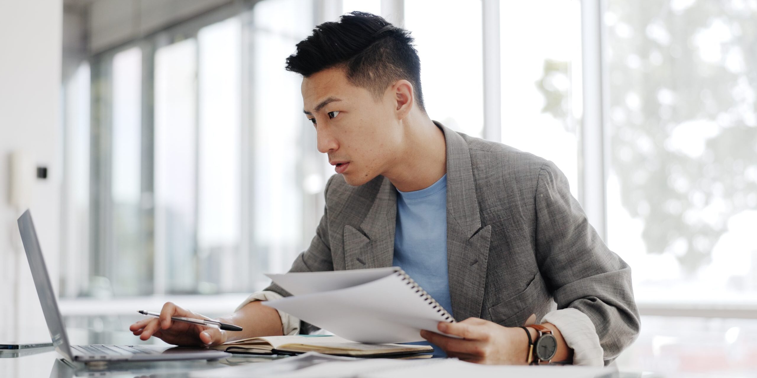 Businessman, writing report and documents at laptop with business plan proposal. Employee, Asian man and working with notes and pen, development and internet for audit and strategy in office