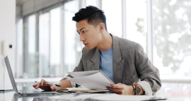 Businessman, writing report and documents at laptop with business plan proposal. Employee, Asian man and working with notes and pen, development and internet for audit and strategy in office