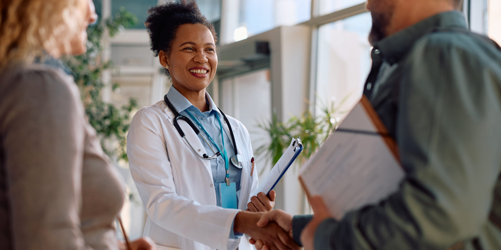 Happy black doctor handshaking with her patients at medical clinic.