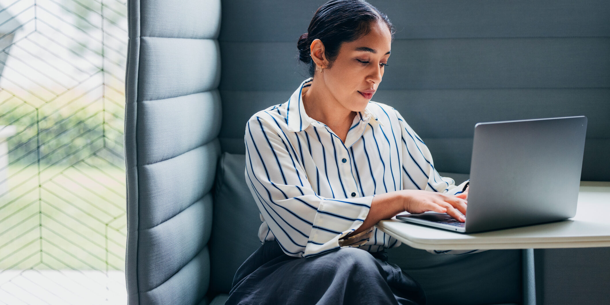 Focused Professional Woman Working on Laptop in a Modern Office Booth